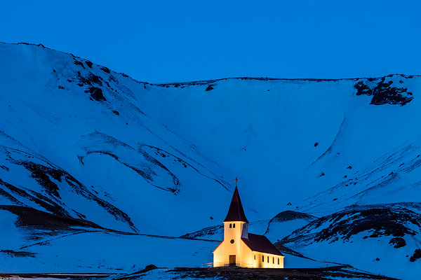 Vik i Myrda church lit up at dusk in Vik, Iceland